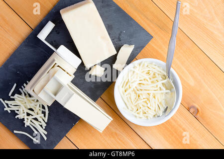 Preparing grated gruyere cheese for cooking with an overhead view of a rotary grater and wedge of cheese on a board alongside gr Stock Photo