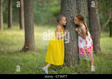 Two little sisters standing talking near a tree in the Park. Stock Photo