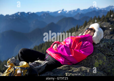 Middle-Aged Woman Relaxes in Warm Winter Sunshine  at 1st Peak on Mount Seymour, BC Canada. Dressed in Colourful Jacket & Toque Stock Photo