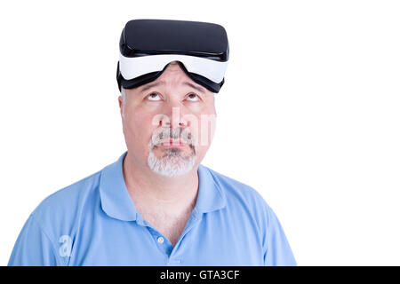 Adult male with virtual reality glasses on his head wearing blue polo shirt against a white background looks up questioning Stock Photo