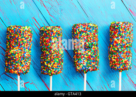Four colorful marshmallows covered with multicolored candy pearls in the colors of the rainbow on a rustic blue wood background Stock Photo