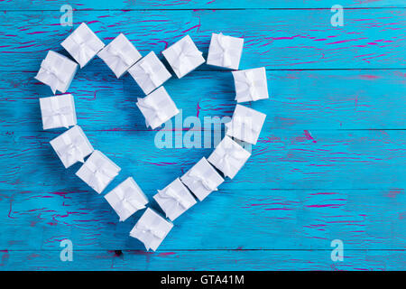 Small gift boxes tied with bows arranged in a heart shape symbolic of love and romance on a rustic blue wood background with cra Stock Photo