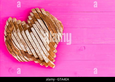 Top down view of freshly baked and sliced heart shaped bread on painted pink wood paneled background with copy space for valenti Stock Photo