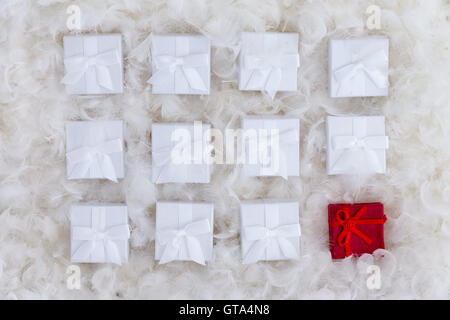 Christmas still life of one red and several white gift boxes nestling on a luxury background of soft fluffy white feathers in a Stock Photo
