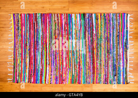 Close up on hand woven rug with red, blue, yellow, purple and other colors over bamboo floor as frame Stock Photo