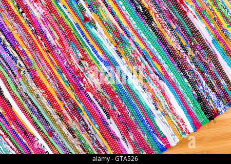 Angled close up on hand woven rug with red, blue, yellow, purple and other colors over bamboo floor with copy space Stock Photo