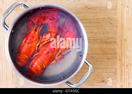 Two red lobsters in a pot of boiling water cooling off on a wooden cutting board after being cooked, viewed from above with copy Stock Photo