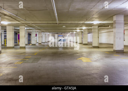 Entrance to a grungy empty covered parking area illuminated by overhead strip lights with a yellow arrow pointing forwards on th Stock Photo