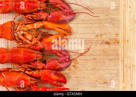 Border of four red lobsters neatly arranged at the side on a wooden cutting board with one upside down to show the underside Stock Photo