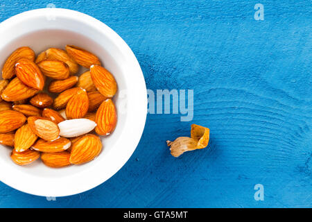 Top down view on whole raw almonds soaked in water over blue wooden table surface. Includes peeled nut skin and copy space. Stock Photo