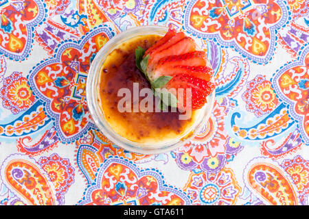 Yummy bowl of creme brulee with fresh strawberries placed on paisley table as seen from an overhead view Stock Photo