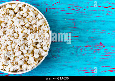 Bowl of freshly made popcorn on a colorful blue crackle paint picnic table as a summer snack, overhead view with copy space Stock Photo