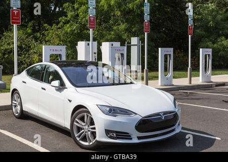 A Tesla Model S automobile gets a charge from a Tesla supercharger charging station at a highway rest stop. Stock Photo