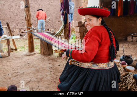 Native Cusquena woman dressed in traditional colorful clothing works on a loom outside her house Stock Photo