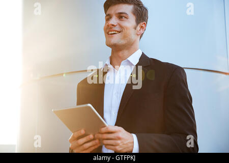 Cheerful attractive young businessman standing outdoors and using pc tablet Stock Photo