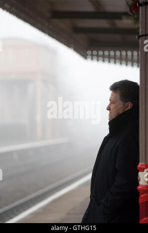 Senior man waiting on a foggy railway station, Cotswolds, UK. Stock Photo