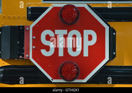 A stop sign on the side of a school bus.  When the bus stops to load or unload students, the sign swings out to make it visible. Stock Photo