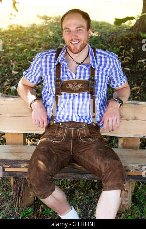 young man sitting on bench in traditional bavarian clothes smiling at camera Stock Photo