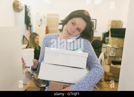 Fashion buyer multitasking carrying shoe boxes, coffee and talking on cell phone Stock Photo