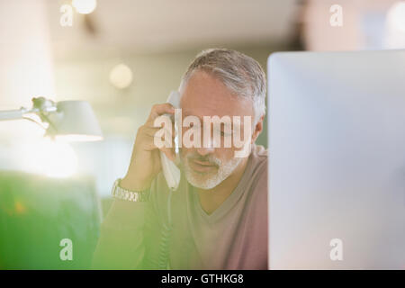 Businessman talking on telephone at computer in office Stock Photo