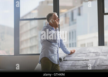 Architect talking on cell phone at blueprints in urban office Stock Photo