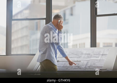 Architect talking on cell phone reviewing blueprints in office Stock Photo