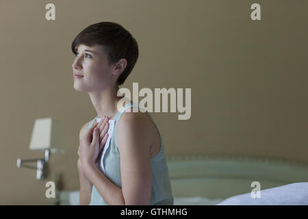 Serene woman clutching letter and looking away in bedroom Stock Photo