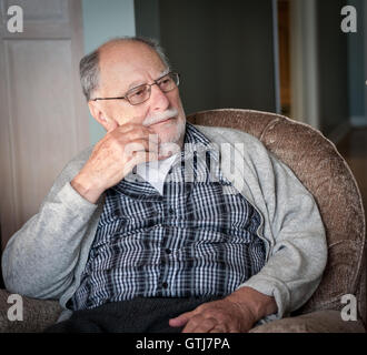 portrait of a grandfather wearing a gray sweater sit on a chair at home Stock Photo