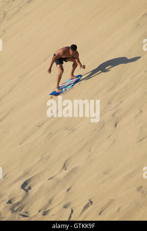 Young man sandboarding in a dune. Spanish coastline. Cadiz. Vertical Stock Photo