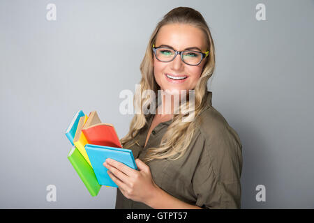 Portrait of a nice happy student girl wearing glasses reading book in the studio over gray background, gain knowledge Stock Photo