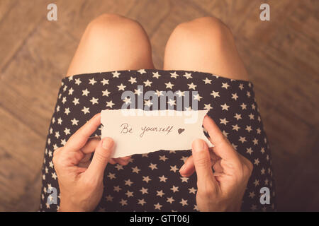 Woman with star patterned dress holding a note with be yourself message on it Stock Photo