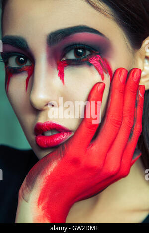 portrait of freak monster with mess dirty colored makeup on her face. crying woman with red bloody tears and hand. Stock Photo