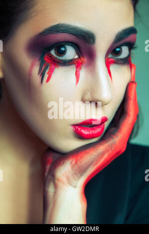 portrait of freak monster with mess dirty colored makeup on her face. crying woman with red bloody tears and hand. Stock Photo