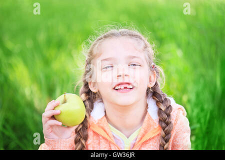 Sweet girl with a fallen toth holding an apple in her hand on nature Stock Photo