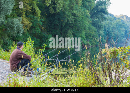 Fishing adventures. Fisherman sitting near the fishing rods waiting to catch a fish Stock Photo