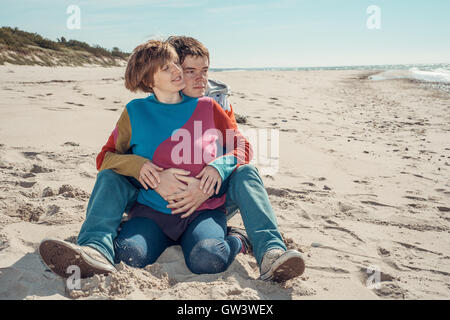 Young man embracing a woman sitting on the beach Stock Photo