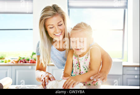 Mother and daughter having fun in the kitchen as the little girl learns to bake helping with kneading the dough Stock Photo