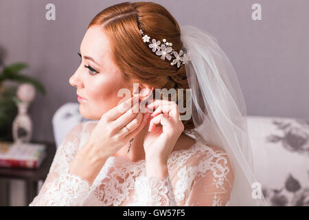 Elegant bride putting on earrings, preparing for wedding Stock Photo