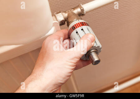 Male hand adjusts heat control on a radiator. Modern house heating technology Stock Photo