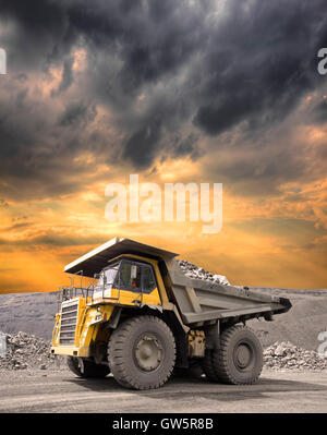 Heavy mining truck driving through the iron ore opencast on stormy sunset Stock Photo