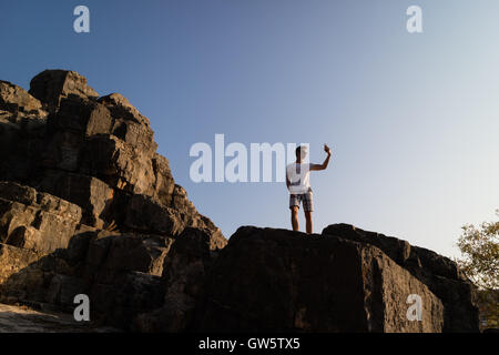 Teenage boy takes a selfie picture / photograph with camera phone on rocky outcrop in sunshine Stock Photo