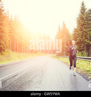 Young fitness woman with long hair running at the rainy morning in mountains. Stock Photo