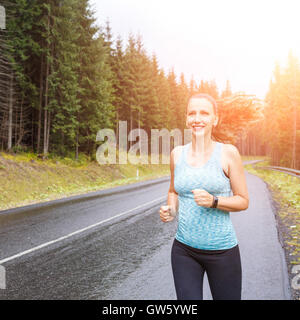 Young fitness woman with long hair running at the rainy morning in mountains. Stock Photo