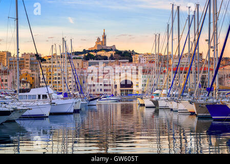 Yachts reflecting in the still water of the old Vieux Port of Marseilles beneath Cathedral of Notre Dame, France, on sunrise Stock Photo