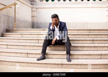 young man sitting on steps in the street with a headache Stock Photo