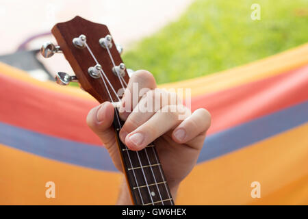 Detail of man relaxing on a hammock and playing ukulele. Stock Photo
