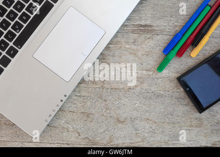 Laptop with mobile phone and some color pens on a wooden table with copyspace. Stock Photo