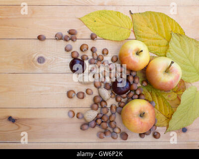 Apples, hazelnuts, chestnut, almonds and fall leaves on the wooden background Stock Photo