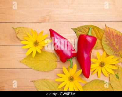 Red bell peppers, yellow topinambour flowers and autumn leaves on the wooden planks background Stock Photo