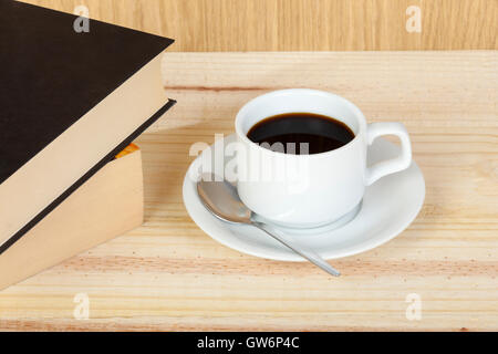 Cup of black coffee on a saucer with a spoon aside two stacked reading books on a wooden table Stock Photo